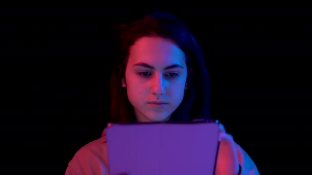 Mujer joven con una tableta. Una mujer está usando una tableta. Luz azul y roja cae sobre una mujer sobre un fondo negro
. - Metraje, vídeo