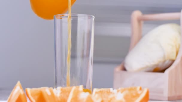 Close-up pouring orange juice in the clear glass on the table with orange sliced on the blurred foreground. - Footage, Video