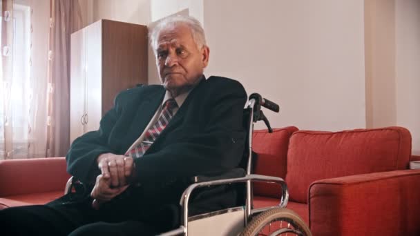 Elderly grandfather - grandfather is sitting in a wheelchair and looking at the camera - Materiał filmowy, wideo