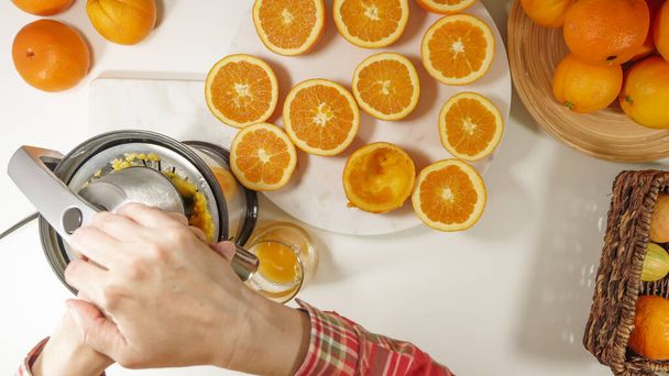 Świeżo wyciśnięty sok pomarańczowy. Biała kobieta wyciskająca pomarańcze za pomocą elektrycznej sokowirówki. Zbliżenie na białym tle, widok z góry - Zdjęcie, obraz