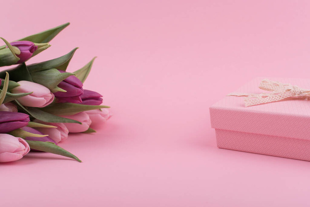 een boeket frisse geurige roze en paarse tulpen en een cadeau voor vrouwendag op een roze achtergrond. Groeten van moeder dag. - Foto, afbeelding