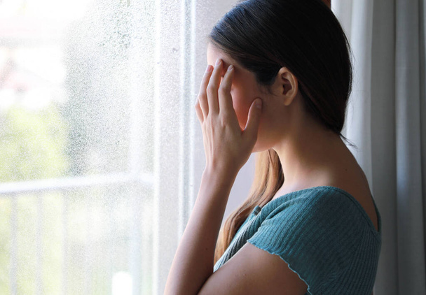 Konzept der saisonalen affektiven Störung. Trauriges depressives Mädchen weint an einem regnerischen Tag zu Hause am Fenster, Fokus auf Modellhand, Innenaufnahme. - Foto, Bild