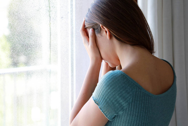 Trauriges depressives Mädchen weint an einem regnerischen Tag zu Hause am Fenster, Fokus auf Modellhand, Innenaufnahme - Foto, Bild