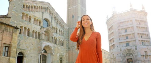 Portrait of beautiful smiling tourist woman in Parma with Cathedral, Bell tower and Baptistery. Panoramic view of traveler girl with Parma, Italy. Parma city is the Italian Capital of Culture 2020. - Photo, Image