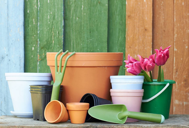Terracotta clay flower pots with black plastic containers and garden tools on wooden table on colorful bright rustic background, nursery and gardening concept, closeup, copy space - Фото, изображение