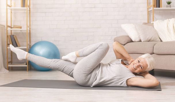 Deportiva mujer mayor haciendo ejercicios abdominales en el suelo en casa
 - Foto, imagen