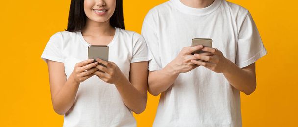 Cropped of asian man and woman using phones over yellow - Fotó, kép