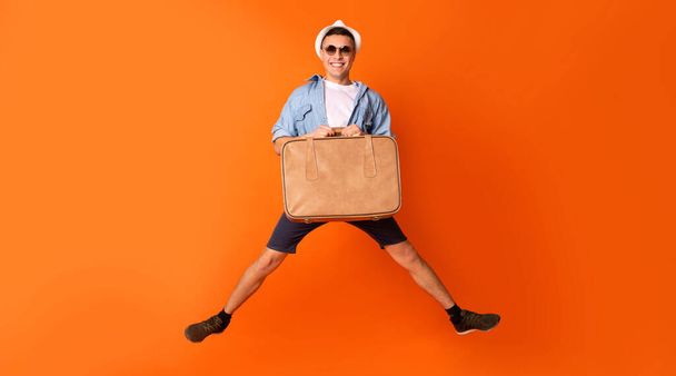 Happy tourist jumping with suitcase over orange background - Fotoğraf, Görsel