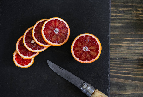 sliced sicilian or bloody oranges on a black slate background  - Photo, Image
