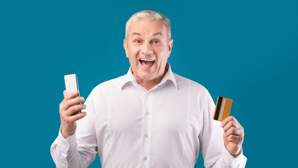 Щасливий зрілий чоловік тримає кредитну картку і мобільний телефон
 - Фото, зображення