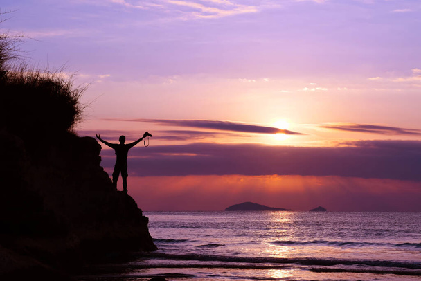 A man standing with a camera on a cliff by the sea at sunrise blue sky background. - Photo, image