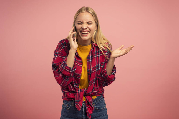 Very happy girl talk with a friend on the mobile phone. Pink studio background. Concept of joyful - Zdjęcie, obraz