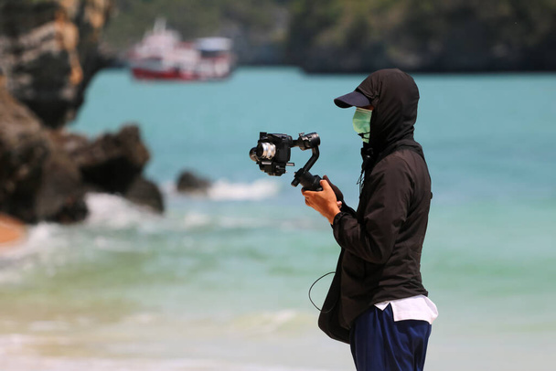 Video fotograf nebo novinář v masce a nahrávání turistických aktivit na pláži během šíření viru korony nebo covid -19. - Fotografie, Obrázek