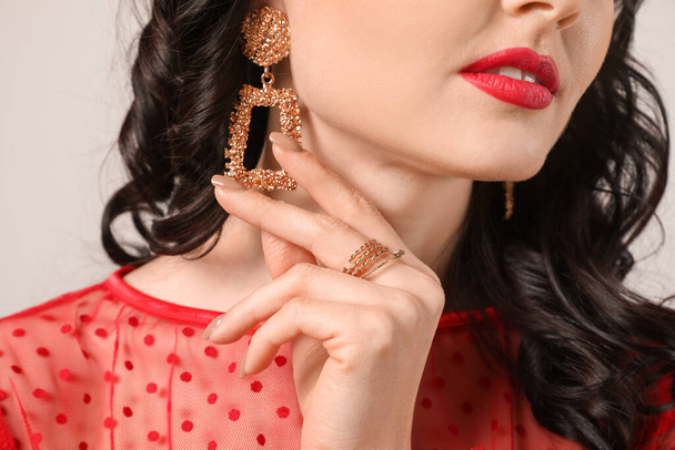 Jonge vrouw met mooie sieraden op lichte achtergrond, close-up - Foto, afbeelding