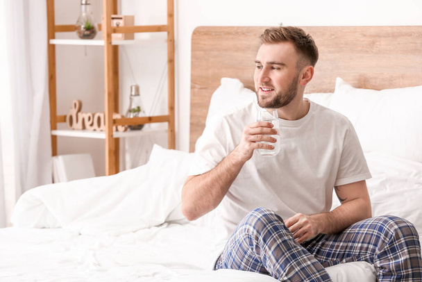 Утром молодой человек пьет воду в спальне
 - Фото, изображение
