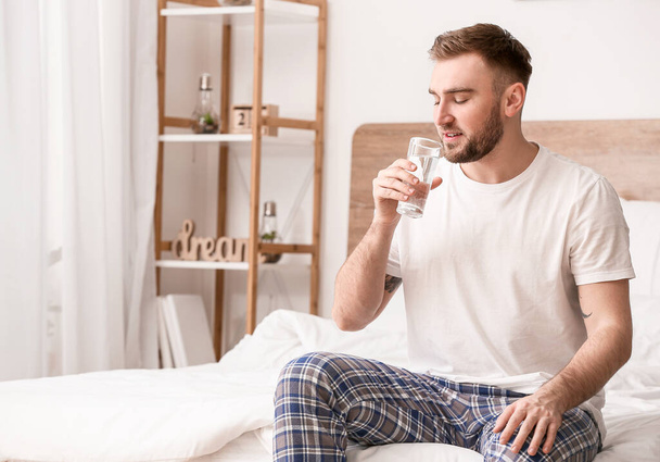 Morning of young man drinking water in bedroom - Photo, Image