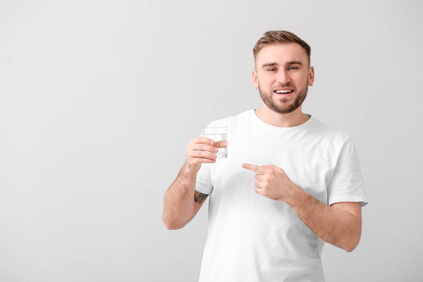 Young man with glass of water on light background - Φωτογραφία, εικόνα