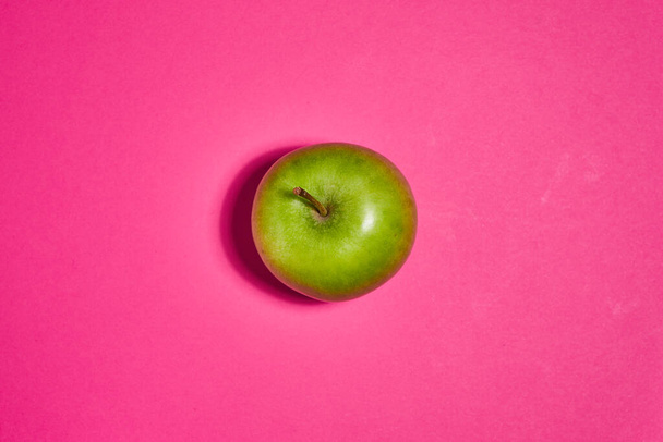 Zöld alma rózsaszín háttérrel. Lapos fekvés, felülnézet, másolás. Élelmiszer-táplálkozási fogalom. - Fotó, kép