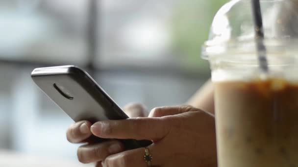 Asian woman using and texting message on mobile smart phone for communication and chatting on social online during drinking a cup of cold drink in coffee shop. - Filmmaterial, Video