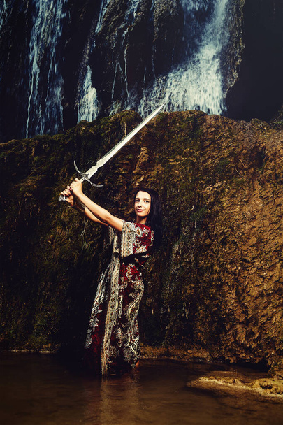 Mujer con espada en el lago cerca de la cascada. - Foto, Imagen