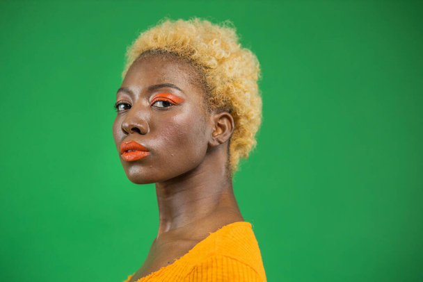 Close-up stylish portrait of an african american model in the center of a green studio. Pleasant fashion and calm female face in a luxurious dark green light indoors - 写真・画像