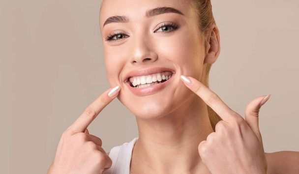 Young Woman Touching Mouth Smiling To Camera On Beige Background - Fotografie, Obrázek