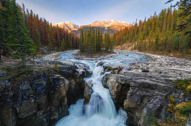 Sunwapta Falls with traveler sitting on rock in autumn forest at sunset. Icefields Parkway, Jasper national park, Canada - Foto, Imagen