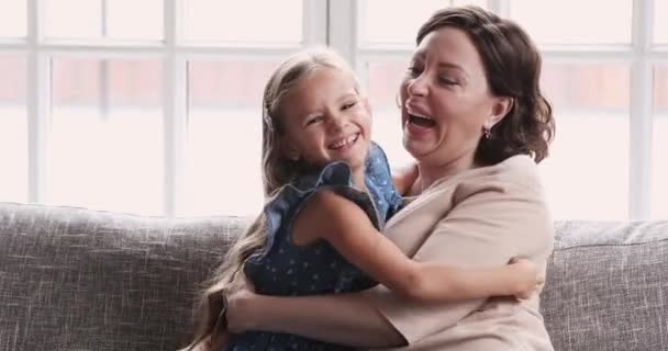 Happy affectionate grandmother and child granddaughter tickling hugging on sofa - Footage, Video