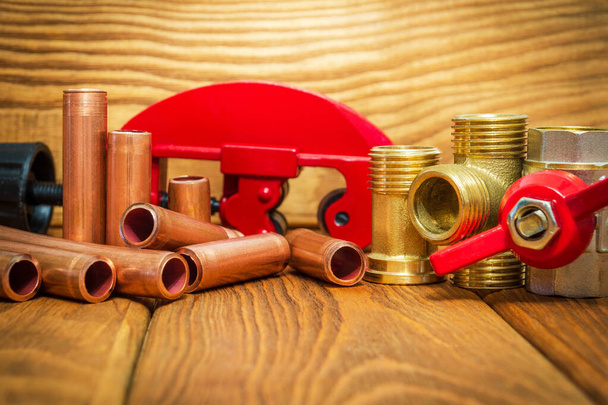 Nueva válvula de bola de agua con mango rojo, accesorios de latón y tubos de cobre para reparaciones de plomería en tableros de madera vintage
 - Foto, imagen