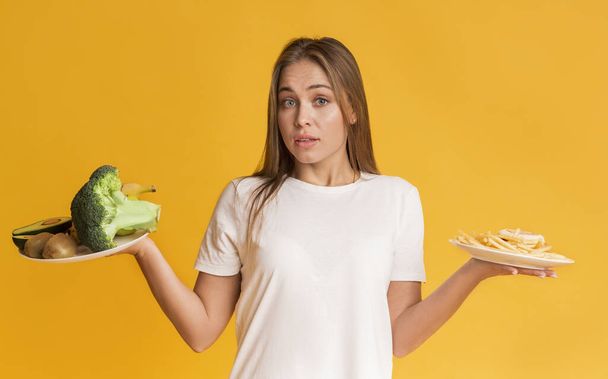 Puzzled Girl Choosing Between Healthy And Unhealthy Food - Foto, Imagen