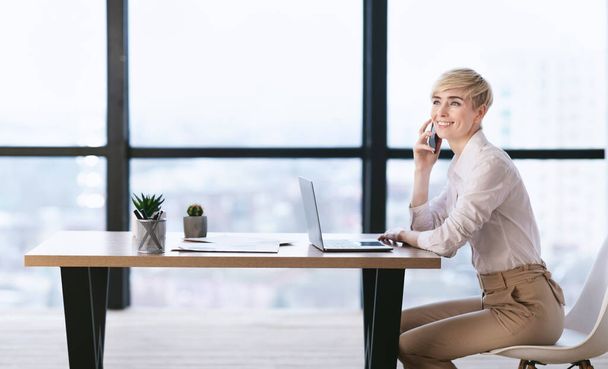 Lady hablando por teléfono móvil sentada en el lugar de trabajo en la oficina
 - Foto, Imagen