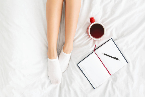 Top view on female legs, notebook and cup of coffee in bed - Foto, afbeelding