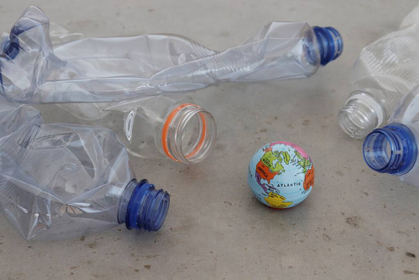 灰色の表面に惑星地球を指しているペットのプラスチックボトル。プラスチック汚染、リサイクル、廃棄物ゼロの概念を示す. - 写真・画像