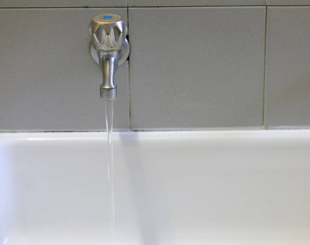 Seramik lavabonun üzerinde içme suyu olan açık çelik musluk. - Fotoğraf, Görsel