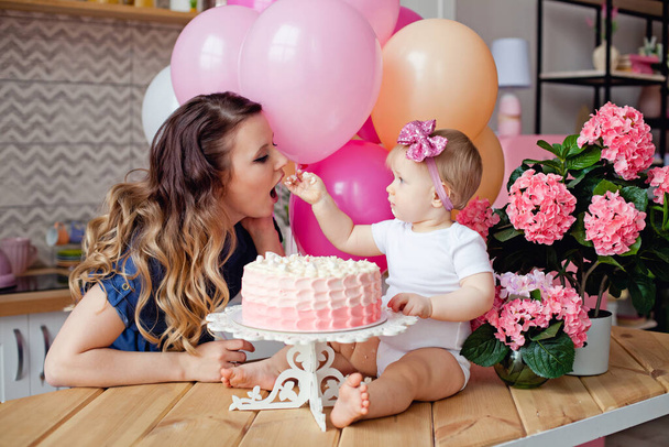 mother and daughter on the table with a birthday cake and balloons - Photo, Image