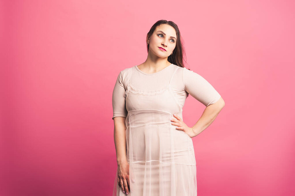 Plus size fashion model in beige dress, fat woman on pink background, body positive concept - Фото, изображение