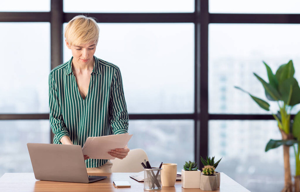 Femme d'affaires occupée lisant des documents d'affaires debout sur le lieu de travail au bureau
 - Photo, image