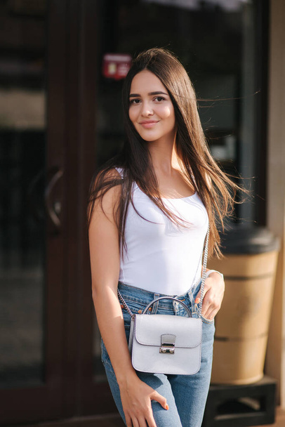 Young and beautiful woman stand outside in front of coffee shop. Attractive brunette in white shirt - Foto, Bild