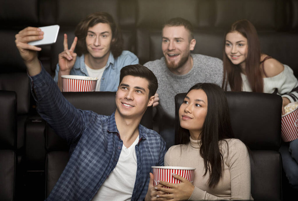 Young friends with mobile phone taking selfie in cinema - Foto, afbeelding