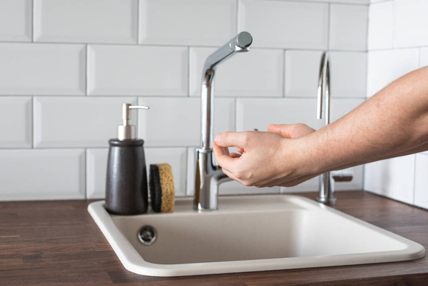Hand washing underwater from a faucet in the kitchen. leanliness, water saving, washing dishes in a bright Scandinavian interior side view - 写真・画像