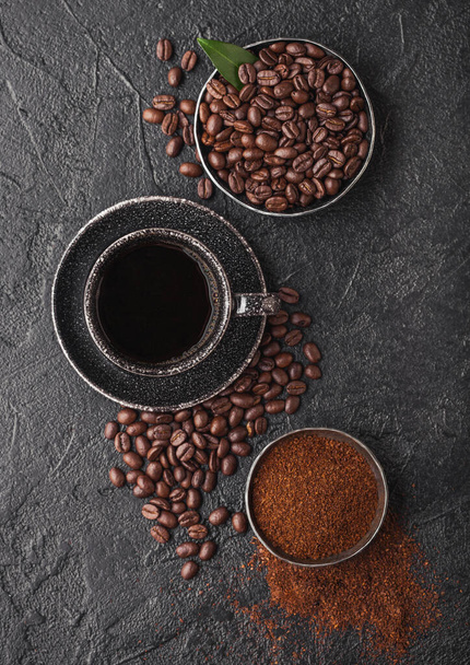 濃い背景にコーヒーの木の葉とサトウキビシュガーキューブと豆や粉と新鮮な生の有機コーヒーのカップ。ブラックセラミックマグカップ - 写真・画像