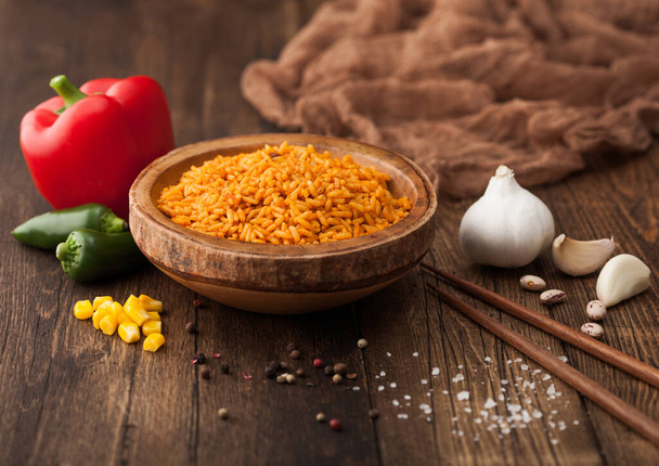 Wooden bowl with boiled red long grain basmati rice with vegetables on wooden background with sticks and red paprika with corn,garlic and basil. - Φωτογραφία, εικόνα