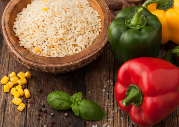 Wooden bowl with boiled long grain basmati rice with vegetables on wooden table background with paprika pepper with corn and basil.  - Photo, Image