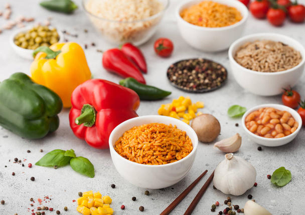 White bowl plates with boiled long grain basmati rice with vegetables and mushrooms on light background with sticks and paprika pepper with corn,garlic and basil with beans and peas. - Foto, Imagen