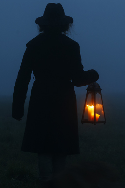 De vrouw houdt een ijzeren lantaarn met kaars in haar handen. mistig landschap op de achtergrond. - Foto, afbeelding
