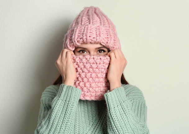 Young woman wearing warm sweater, snood and hat on light background. Winter season - Foto, imagen