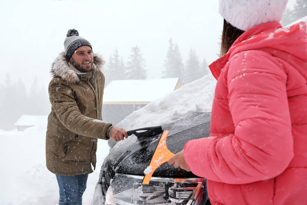 Young couple cleaning snow from car outdoors on winter day - Foto, Imagem