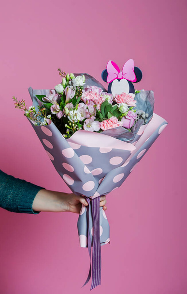 Gyönyörű csokor virág csomagolásban egy női kéz rózsaszín háttér. Divatos transzparens Valentin-napra, nemzetközi nőnapra vagy anyák napjára. - Fotó, kép