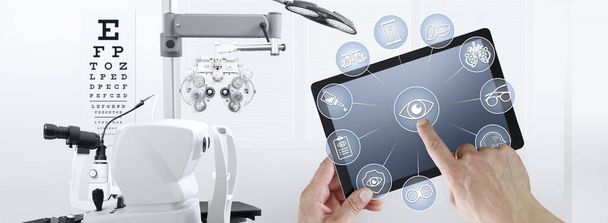 χέρια οθόνη αφής του ψηφιακού tablet με οφθαλμίατρος και εικονίδια οφθαλμίατρος σύμβολα, οφθαλμολογία και οπτομετρικός εξοπλισμός στο παρασκήνιο - Φωτογραφία, εικόνα