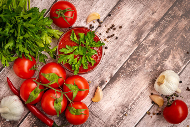 Bright, juicy, ripe tomatoes on a branch lie around ketchup in a sauce bowl on a wooden table with herbs, garlic, hot and allspice. - Fotoğraf, Görsel